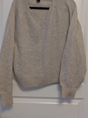 Beige stickad tröja med v-ringning - Mysig beige stickad tröja med djup v-ringning och långa ärmar. Tröjan har ribbstickade muddar vid ärmslut och nederkant. 