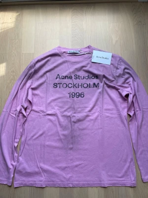 Ljusrosa långärmad topp Acne Studios - Långärmad topp från Acne Studios i en ljusrosa färg med tryck 'Acne Studios STOCKHOLM 1996' framtill. Klassisk rund halsringning och avslappnad passform. Perfekt för dig som gillar minimalistisk och stilren design. Aldrig använda och tag kvar.