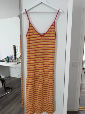 Randig långklänning från Zara - Färgglad långklänning från Zara med smala axelband och v-ringning. Klänningen har ett stickat mönster i rött, gult och vitt med vågiga ränder. Perfekt för varma dagar och ger en retrovibe till din outfit.