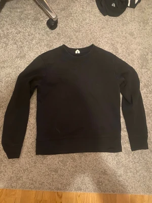 Svart sweatshirt från arket  - En stilren svart sweatshirt från arket med rund halsringning och ribbade muddar vid ärmslut och nederkant. Tröjan är enkel och passar perfekt till jeans eller joggers. Tillverkad i mjukt material för maximal komfort.