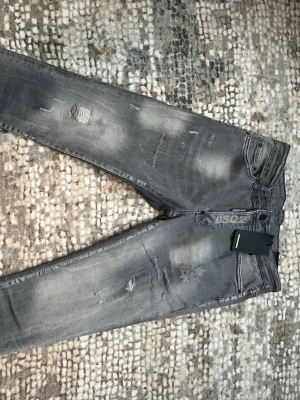 Grå slitna jeans från Dsquared2 - Säljer ett par grå jeans från Dsquared2 med slitningar och tvättade detaljer. Modellen har smal passform, klassiska fem fickor och synliga slitningar på både fram- och baksida. 