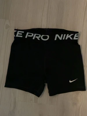 Svarta Nike Pro träningstights shorts - Säljer ett par svarta Nike Pro shorts med bred resår i midjan där det står 'NIKE PRO' i vitt. Tight passform och är i 146/156 lite trådar 
