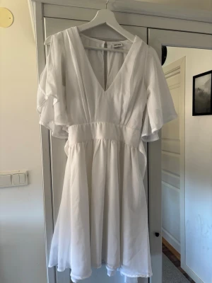 Vit omlottklänning med v-ringning - Säljer en vit kortklänning från bubbelroom med v-ringning och omlottdetalj. Klänningen har vida, korta ärmar och ett knytband i midjan.