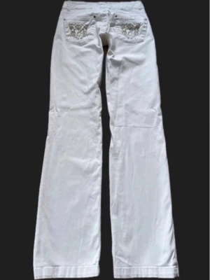 Vita bootcut jeans med broderi - Vita low waist jeans i bootcut/straight modell med snygga broderade gulddetaljer på bakfickorna. Storlek står 38 men måtten lyder så här: Midjemått: 35 cm. Innerbenslängd: 80 cm. Gren: 20 cm. Lite stretchigt material. Inte denimtyg (Jeansen passar inte mig kan ej fotas på)