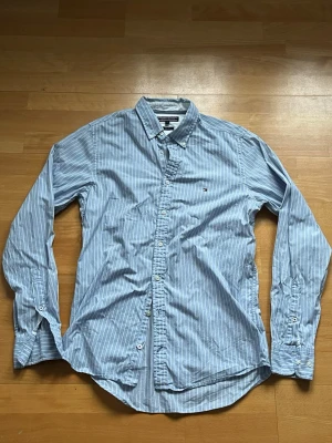 Tommy Hilfiger skjorta ( storlek m )  - En riktigt fet ljusblå randig Tommy Hilfiger skjorta. Nästan aldrig använd dessutom inga defekter. Väldigt snygg skjorta om man vill se lite stilligare ut. Priset ej hugget i en sten