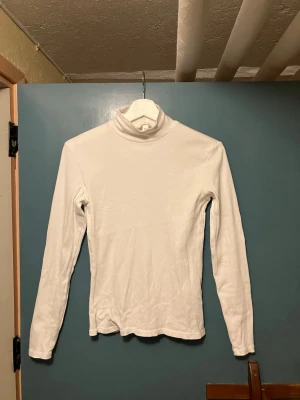 Vit ribbad polotopp från H&M - Vit långärmad polotopp från H&M i ribbad bomull. Tight passform och hög krage som ger en clean och stilren look. Perfekt att bära som lager eller för sig själv.