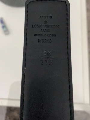 Svart  monogram skärp - Snyggt svart skärp med klassiskt monogrammönster och stor i guld som spänne. Tillverkat i Spanien och gjort av exklusivt skinn. Perfekt accessoar för att lyfta vilken outfit som helst.