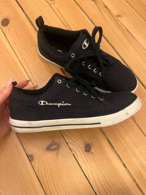  Champion sneakers storlek 42 nya - Snygga sneakers från Champion med klassisk låg profil och vita detaljer på sulan. Skorna har snörning och är tillverkade i textilmaterial med broderad Champion-logga på sidan och tungan. Perfekta för en avslappnad streetstyle-look.