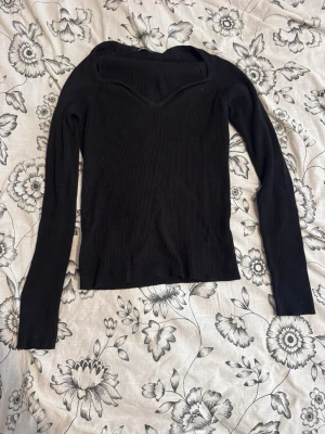 Svart ribbad långärmad topp - Snygg svart ribbad topp med lång ärm och unik v-ringad halsringning. Toppen är figurnära och har en croppad känsla, perfekt att styla till jeans eller kjol. Materialet är stretchigt och bekvämt, vilket gör den enkel att bära hela dagen.