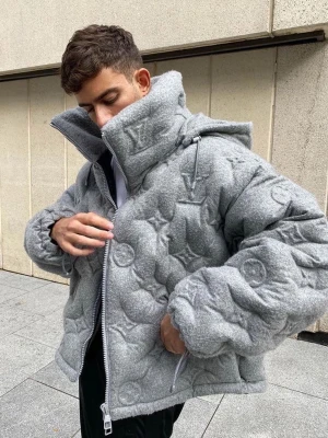 Grå pufferjacka från Louis Vuitton - Säljer en grå pufferjacka från Louis Vuitton med ikoniskt LV-monogram i quiltat mönster. Jackan har hög krage, dragkedja framtill, justerbar huva och muddar med dragsko. Perfekt för dig som vill sticka ut med en lyxig och trendig vinterjacka.