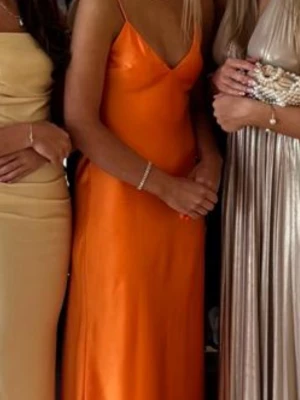 Orange långklänning med smala axelband - En orange långklänning med smala axelband och v-ringning. Klänningen har en slät, glansig yta och en figurnära passform som ger en elegant siluett. Perfekt för sommar och bal🧡