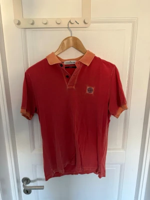 Röd kortärmad pikétopp Stone Island - Röd kortärmad pikétopp från Stone Island med orange krage och ärmslut. Klassisk knappslå framtill och ikonisk logga på bröstet. För mer frågor eller intresse av fler bilder är det bara att höra av sig🤠