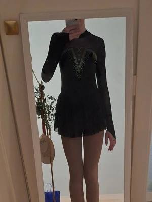 Svart konståkningsklänning med kristaller - Säljer denna ikoniska konståkningsklänningen från märket iEFiEL köpt från Joom för ca 200kr. Strl 158/164 (13-14 år) Använd 1-2 gånger på tävling så den är nästan helt ny. Säljer pga den är lite för liten och jag har köpt nya klänningar. 