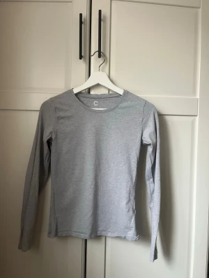 Ljusgrå långärmad topp - En enkel och stilren ljusgrå långärmad topp med rund halsringning. Tillverkad i mjuk bomullsmix, perfekt för lager på lager eller att bära som den är. Passformen är normal och toppen har en minimalistisk look utan synliga detaljer.