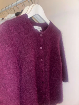 Vinröd stickad kofta från & Other Stories - Supermjuk och fluffig vinröd/lila kofta från & Other Stories med rund halsringning och knappar framtill. Koftan har en rak passform och är tillverkad i ett mohairliknande material .köpt för ca 8-900. Inga tecken på användning och använd ca 2ggr