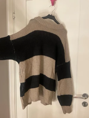 Beige och svart randig stickad tröja - Stickad tröja från 157 i beige och svart med breda horisontella ränder. Oversized passform med rundad, ribbstickad halsringning och långa ärmar. 