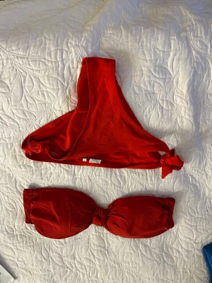 Röd bandeau bikini med knyt - Snygg röd bandeau bikini med knyt både på toppen och trosorna. Bikinin har en enkel och stilren design utan mönster, perfekt för strandhäng eller poolparty. Materialet känns mjukt och följsamt mot huden.