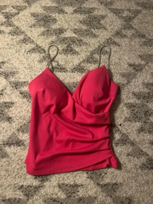 Rosa ribbad linnetopp med smala band - Trendig rosa linnetopp med smala axelband och ribbad struktur. Toppen har en v-ringad skärning och croppad passform som ger en snygg siluett. Perfekt att styla med jeans eller kjol för en cool look. Köpte för 150 