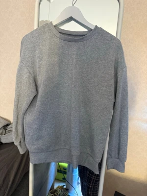 Grå basic sweatshirt - En enkel grå sweatshirt med rund hals och långa ärmar. Tröjan har ribbade muddar vid ärmslut och nederkant. Perfekt för en avslappnad stil och lätt att matcha med andra plagg.