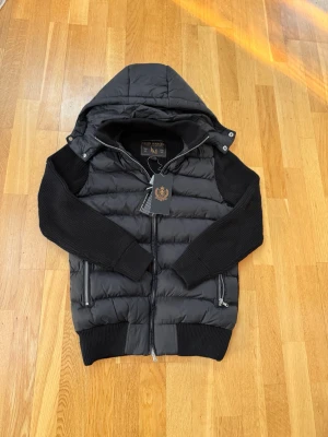 Leon Marcél Hybrid Jacka – Svart | Avtagbar Huva - Premium hybridjacka från Leon Marcél med avtagbar huva och microfleece-fodrade fickor. Toppskick. Finns även i alla storlekar på cain.se – betala med Klarna.​​​​​​​​​​​​​​​​