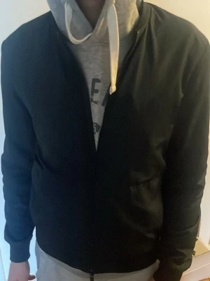 Mörk blå bomberjacka med ribbade muddar - Stilren mörk blå bomberjacka med klassisk passform och ribbade muddar vid ärmslut och midja. Jackan har dragkedja framtill och två sidofickor. Perfekt för dig som gillar en enkel och clean look. Materialet känns mjukt och lätt.