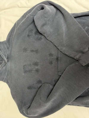 Grå hoodie från Axel Arigato med brodyr - Säljer en grå hoodie från Axel Arigato med stora broderade bokstäver på bröstet. Klassisk modell med huva och ribbade muddar vid ärmar och nederkant. Tillverkad i mjukt bomullsmaterial som är skönt att ha på sig. Den är lite oversized 