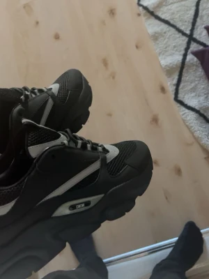Svarta Dior B22 - Snygga svarta Dior sneakers med vita och grå detaljer. Skorna har en chunky sula och ovandel i mesh och syntetmaterial för en sportig vibe. Klassisk snörning och diskret Dior-logga på sidan. Perfekta för dig som gillar streetwear och exklusiva märken.