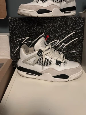 Air Jordan 4 Retro White/Black - Snygga Air Jordan 4 Retro sneakers i vitt och svart med meshpaneler och detaljer i grått. Skorna har en ikonisk siluett med synlig Air-enhet i sulan och klassiska plastdetaljer vid snörningen. Ovandelen är i läder och textil för en clean och sportig look. Använt de bara 2 gånger så de är i fint skick. Skriv för ytterliga bilder eller info.