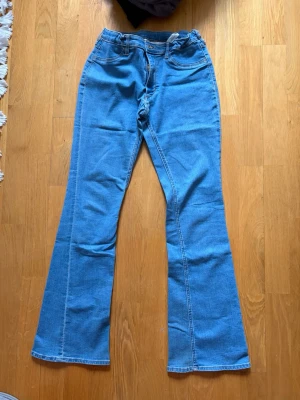 Blåa flare jeans från H&M - Säljer ett par ljusblåa flare jeans från H&M med låg midja och justerbar midja. Klassisk femficksmodell i mjuk denim med utsvängda ben. Perfekta för dig som gillar retrostil och vill ha ett par bekväma och snygga jeans.
