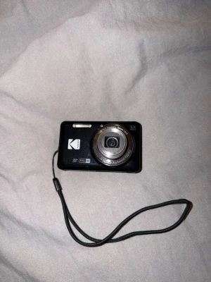 Svart Kodak digitalkamera med handledsrem - Säljer min svarta kodak pixpro x55. Inköpspris 1990. Inte haft den i mer än ett år men ska köpa en dyrare kamera så behöver inte denna längre. Inga fel på den. Simkort medföljer plus laddare och fodral.