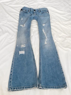 Ljusblå slitna superlågmidjade bootcut jeans - Sååå sjukt snygga superlågmidjade vintage bootcut jeans från Hollister!! 😩😩🙏🏼💓säljer eftersom de inte passar därför har jag heller ingen bild på! 💓 Midjemått: 36 cm Innebenslängd: 78 cm 