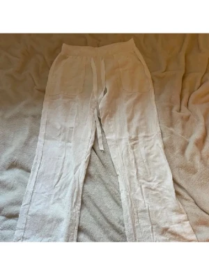 Vita linnebyxor - Säljer ett par vita linnebyxor med bred resår i midjan och dragsko. Byxorna har raka ben och två stora fickor framtill. Perfekta för en avslappnad och stilren look. Materialet är luftigt linne som känns svalt och skönt.