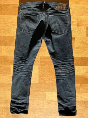 Limited edition RRL selvege slim bootcut jeans - Tillverkade i USA av 15 oz amerikansk selvedge-denim. Modellen på bilden: Är 190 cm lång och väger 82 kg. Det är en limiterad utgåva som kostade ~ 4000 kr från ralph lauren. Storlek: W34 L34 Mått: Midja (mätt plant): 45 cm Total längd: 115 cm Benöppning: 21 cm