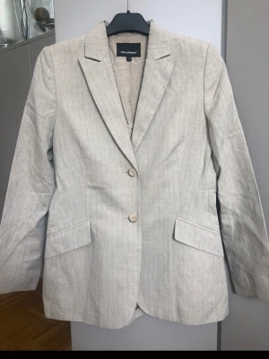 Beige kavaj 36 - Snygg beige kavaj från Mari Philippe  med diskret mönster och två knappar framtill. Klassisk passform med två fickor och krage. Perfekt för att höja din outfit med en stilren touch. Materialet känns lätt och bekvämt.