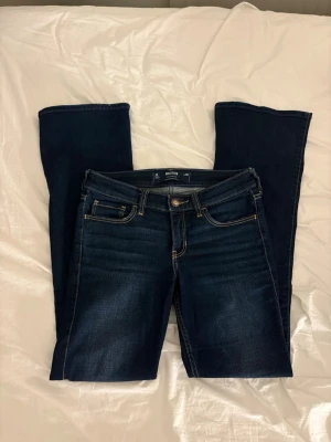 Bootcut jeans - Snygga mörkblå bootcut jeans från Hollister med klassiska fem fickor och kontrastsömmar. Jeansen har en läderpatch med logga bak och är tillverkade i stretchigt denim för skön passform. Perfekta till sneakers eller boots.