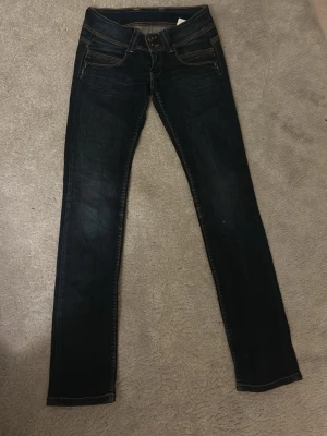 Mörkblå skinny jeans med dubbla knappar - Snygga mörkblå skinny jeans med dubbla knappar i midjan och kontrastsömmar. Jeansen har klassiska fem fickor och en smal passform som sitter tajt längs benen. Perfekta för en trendig och avslappnad look.