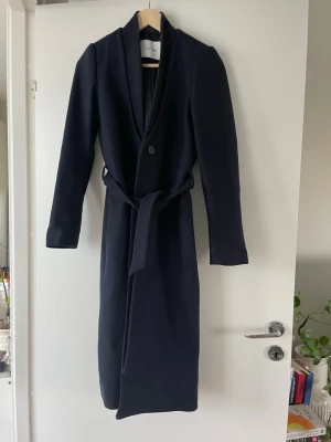 Mörkblå lång kappa från IVY OAK - Stilren mörkblå kappa ä med knytband i midjan och tre knappar framtill. Kappan har en rak, lång siluett. Elegant och minimalistisk 💖passar dig som är lång (för lång för mina 159 cm 😅) storlek 32, men skulle säga den passar XS/S (34-36) knappt använd pga dess långa passform!