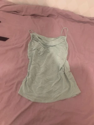 Ljusgrön linnetopp med tunna band - Snygg ljusgrön linnetopp med tunna axelband och draperad ringning. Perfekt till sommaren och enkel att matcha med jeans eller kjol. Materialet känns mjukt och lätt, vilket gör toppen superbekväm att bära. En liten håll i den