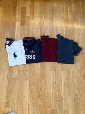 Fyra pikétröjor från Polo Ralph Lauren och morris - Säljer fyra pikétröjor från Polo Ralph Lauren i olika färger: vit med stor logga, marinblå med brodyr och text, vinröd samt mörkgrå. Alla har klassisk krage, knappar framtill och korta ärmar. Perfekta för en stilren och sportig look.