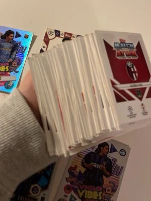 Stort paket fotbollssamlarkort - Säljer ett stort paket med fotbollssamlarkort från Topps Match Attax-serien. Bland korten finns flera holografiska och specialkort med motiv från Champions League, bland annat Vintage Vibes och Trophy Triumph. Perfekt för samlare som gillar fotboll och unika kort.