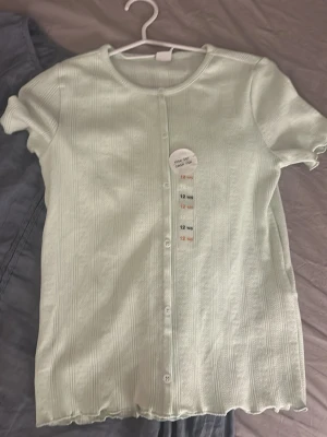Ljusgrön ribbad topp med knappar - Söt ljusgrön topp med ribbad struktur och korta ärmar. Aldrig använd och köpt utomlands 