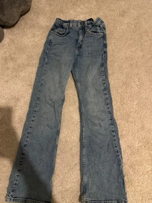 Blå bootcut jeans med fem fickor - Ett par klassiska blå bootcut jeans i denim med fem fickor och normalhög midja. Jeansen har dragkedjegylf och knapp framtill samt dubbla bakfickor. Perfekta för en avslappnad och tidlös look.