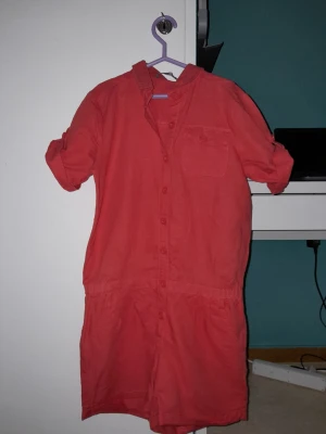 Röd byxdress shorts - Röd byxdress shorts med bröstficka med knapp och bakfickor med knappar. Härlig för en sommarkväll eller nåt mer. Styla den!!