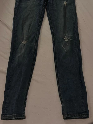 Mörkblå slitna jeans med raka ben - Mörkblå jeans med raka ben och slitningar på både lår och knän. Jeansen har en klassisk femficksmodell och är tillverkade i denim. Perfekta för en avslappnad och trendig look.