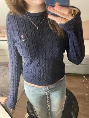 Mörkblå kabelstickad tröja Bondelid  - Säljer en mörkblå kabelstickad tröja från Bondelid med broderad logga på bröstet. Tröjan har rund halsringning, långa ärmar och ribbade muddar. Perfekt för dig som gillar klassisk och stilren look.