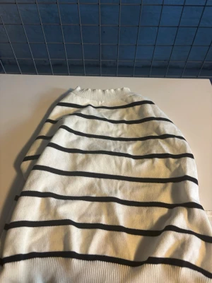 Linnetopp öppen rygg - Snygg vit linnetopp med svarta horisontella ränder och knytband i sidorna. Toppen har ribbad kant upptill och nertill och är ärmlös, perfekt för en chill och trendig look.Öppen i ryggen