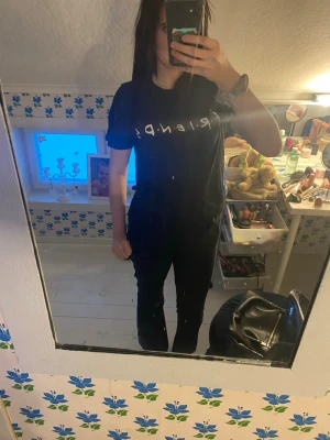 Svart Friends t-shirt - Säljer en svart t-shirt med vit Friends-logga över bröstet. T-shirten har korta ärmar och en klassisk passform som är enkel att matcha. Perfekt för dig som gillar tv-serien Friends och vill ha en stilren look.