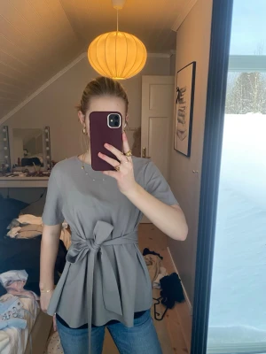 Grå topp med knytband - Säljer en snygg grå topp med korta ärmar och ett stort knytband i midjan. Jag har köpt den på vinted men är ursprungligen från Shein🥰 Inge skador eller tecken på användning. 