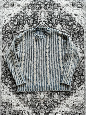 Blåvit kabelstickad tröja - Säljer en blåvit kabelstickad tröja med rund hals och ribbade muddar. Tröjan har ett snyggt randigt mönster med inslag av grova flätor och är gjord i ett tjockare garn som känns riktigt skönt. För mer info är det bara att skriva! Storlek M!