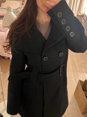 Medel lång svart fin kappa med skärp - Super fin och skön medel lång kappa med fint skärp och fina detalj knappar även knappar som man kan stänga med framm.  Katter finns i hemmet 